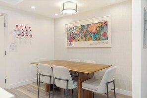 A modern dining area with a wooden table and grey chairs, a colorful abstract painting, and a red spherical decoration on the wall. - Villa Cortina 135 | 2BR Vail Village Retreat with Pool (Vail)