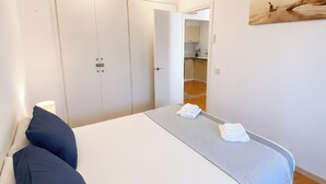 Ein Schlafzimmer mit Bett, Kissen, Deckenventilator, Wandkunst und einem durchgegangenen Türrahmen sichtbaren Badezimmer.