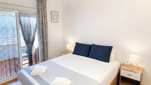 Ein Hotelzimmer mit Bett, Deckenventilator, Nachttisch mit Lampe und Blick ins Freie durch ein Fenster mit Vorhängen.