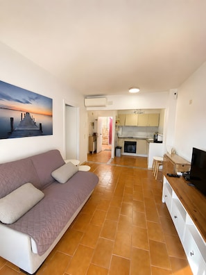 A living room with a sofa, a television, and a kitchen in the background. - Holiday Home 'Can Vera Port' with Mountain View, Wi-Fi, and Air Conditioning (Llançà)