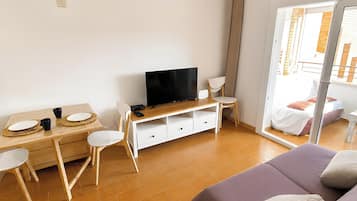 A room with a bed, a TV, a desk with chairs, and a sliding glass door to a balcony.