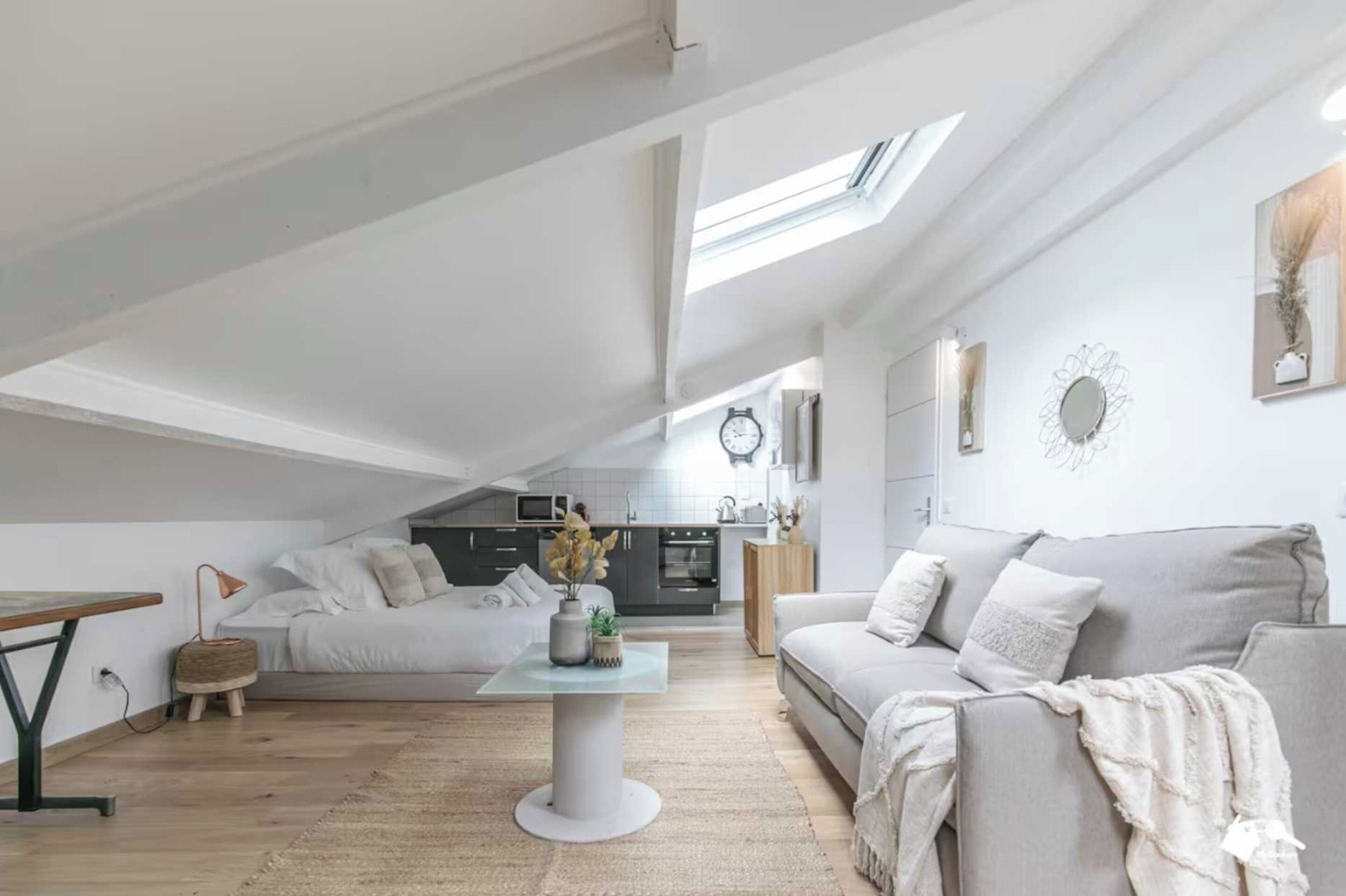 A spacious loft with a high ceiling, a dining area, a living room with a sofa and a coffee table, and a kitchen in the background.