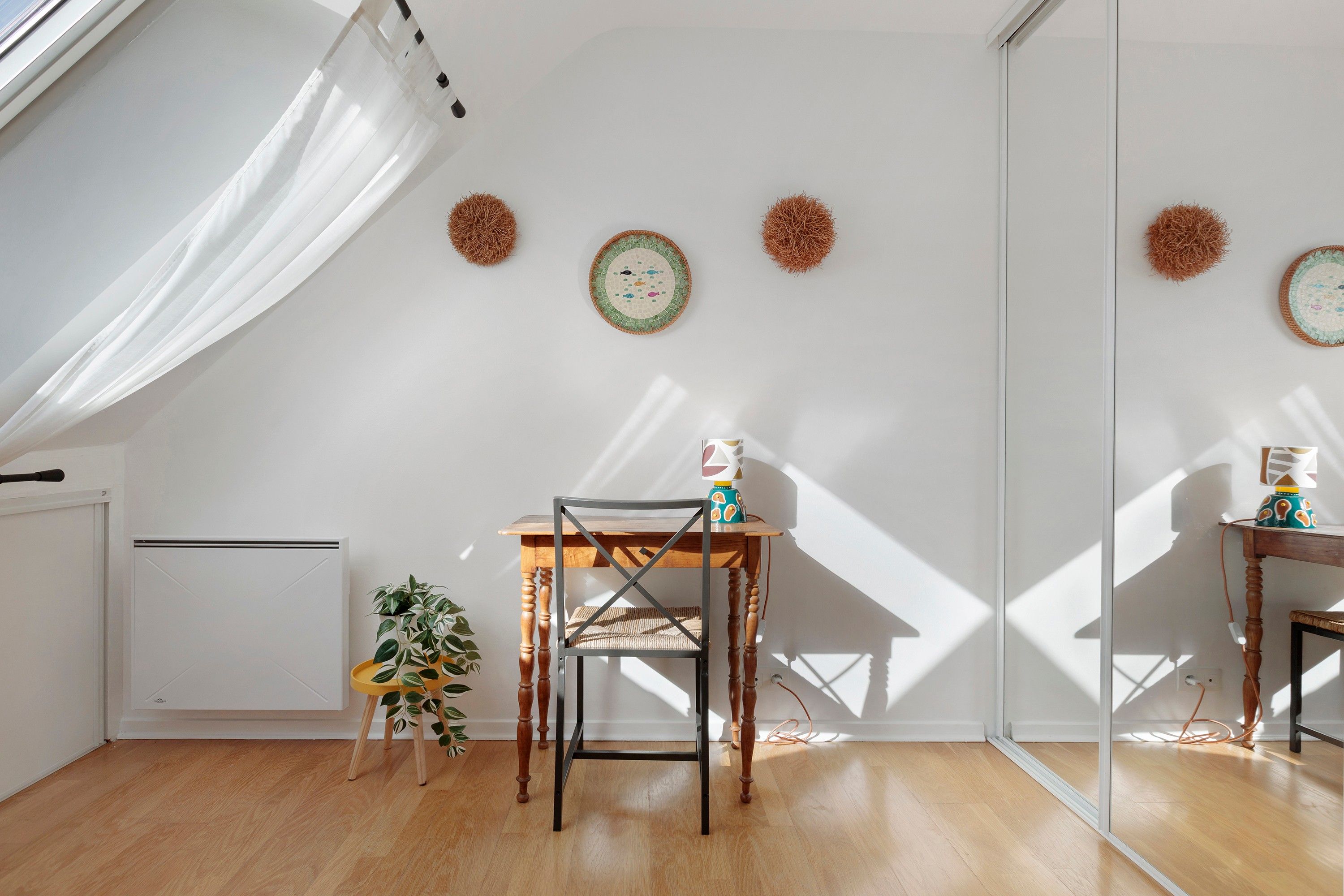 A room with a wooden floor, a table with a chair, a radiator, and wall decorations.