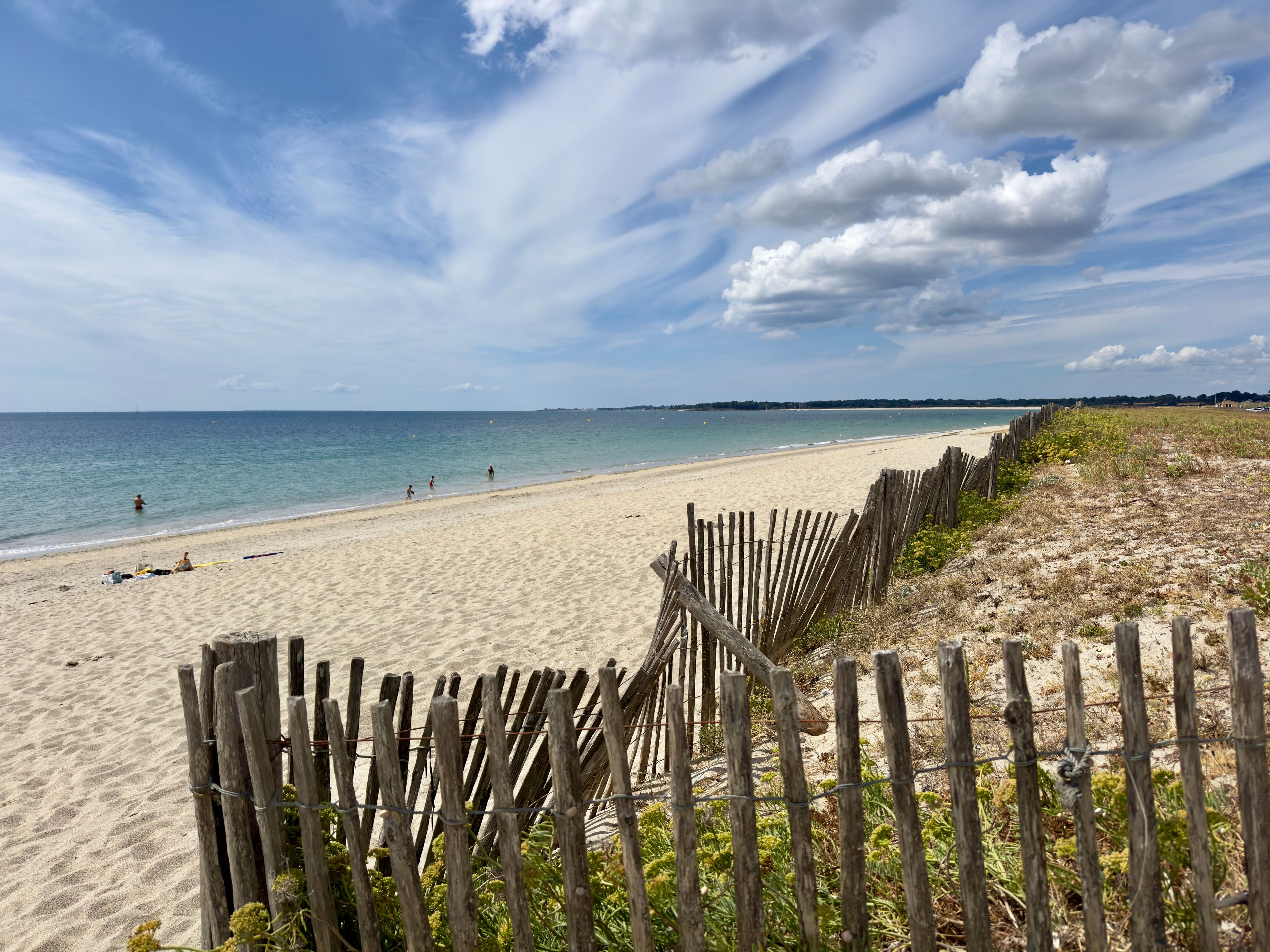 A beach with a wooden fence, sandy shore, and a clear sky.
