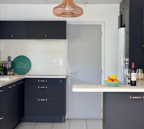 Una cocina moderna con armarios oscuros, una encimera blanca, un plato decorativo verde y una botella de vino.