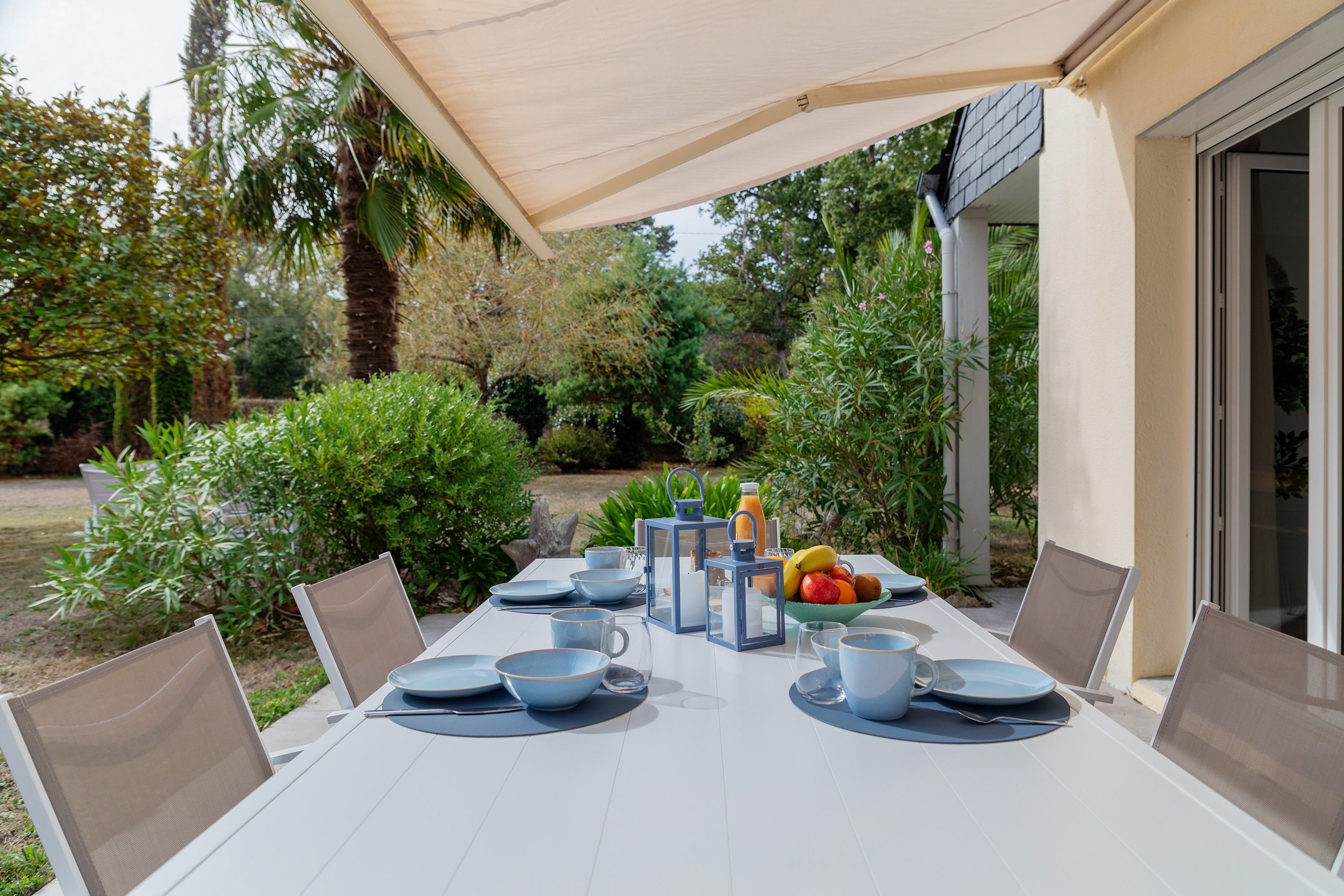 An outdoor dining area with a table set for four, surrounded by chairs, and a table umbrella providing shade.
