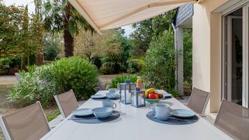 An outdoor dining area with a table set for four, surrounded by chairs, and a table umbrella providing shade.