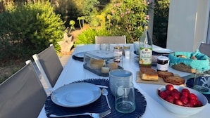 An outdoor dining table set with plates, cutlery, a bottle of juice, a bowl of strawberries, and a basket of bread. - Kerlevenan House: A Peaceful Haven in the Heart of the Rhuys Peninsula (Sarzeau)