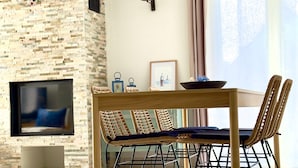 A modern living room with a stone wall, a flat-screen TV, a dining table with chairs, and a hanging light fixture. - Kerlevenan House: A Peaceful Haven in the Heart of the Rhuys Peninsula (Sarzeau)