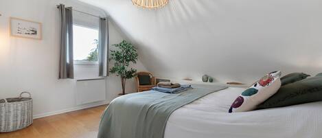 Un dormitorio con cama, lámpara colgante, ventana con cortinas, una planta y un radiador fijado a la pared.