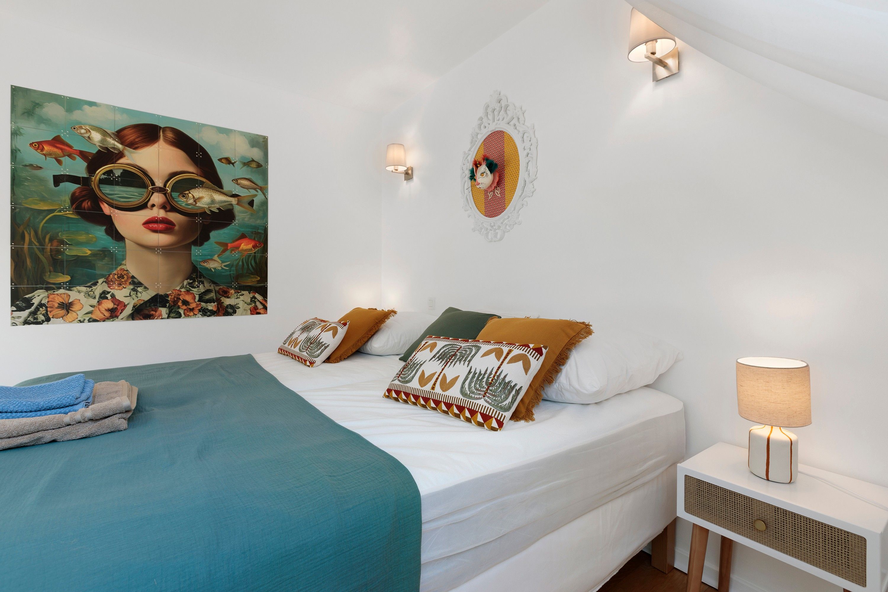 A modern bedroom with a bed, pillows, a nightstand, a lamp, and a wall art piece.