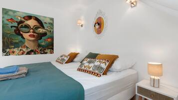 A modern bedroom with a bed, pillows, a nightstand, a lamp, and a wall art piece.
