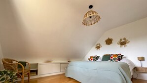 A bedroom with a bed, a chair, a hanging light fixture, and a wall with decorative elements. - Kerlevenan House: A Peaceful Haven in the Heart of the Rhuys Peninsula (Sarzeau)