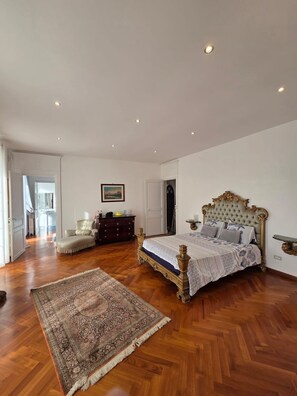 Ein geräumiges Schlafzimmer mit einem großen Bett, Holzboden, einem dekorativen Teppich und einem Schminktisch.