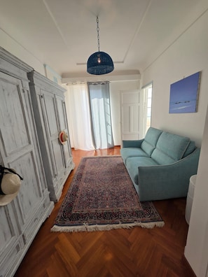 Ein Zimmer mit einem blauen Sofa, einem gemusterten Teppich und einem weißen Kleiderschrank.