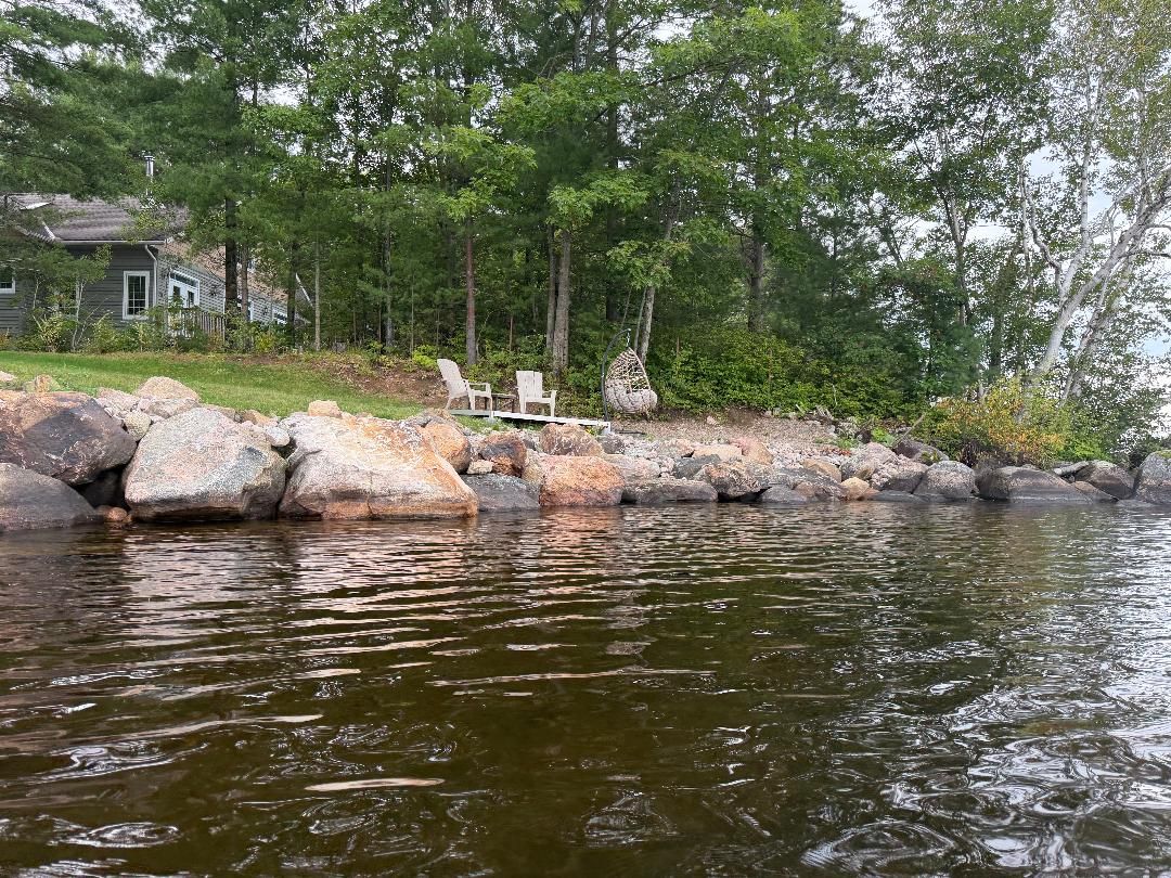A lakeside property with a house, large rocks, and a chair by the water.