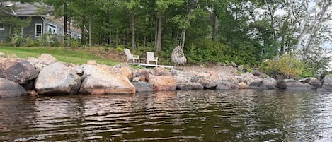 A lakeside property with a house, large rocks, and a chair by the water.