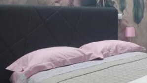 Ein Bett mit dunkelbrauner Kopfstütze, einem rosafarbenen Kissen und einer gesteppten Bettdecke.