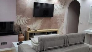 Ein modernes Wohnzimmer mit einem grauen Sofa, einem flachbildfernseher an der Wand, einem Couchtisch aus Holz und einer dekorativen Wandverkleidung.