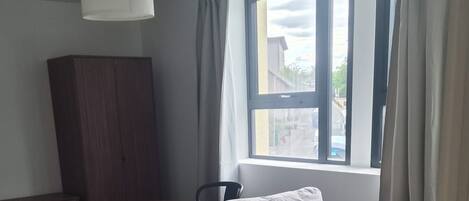 A neutral-colored sofa, a small table, and a window with curtains in a room with a carpeted floor.