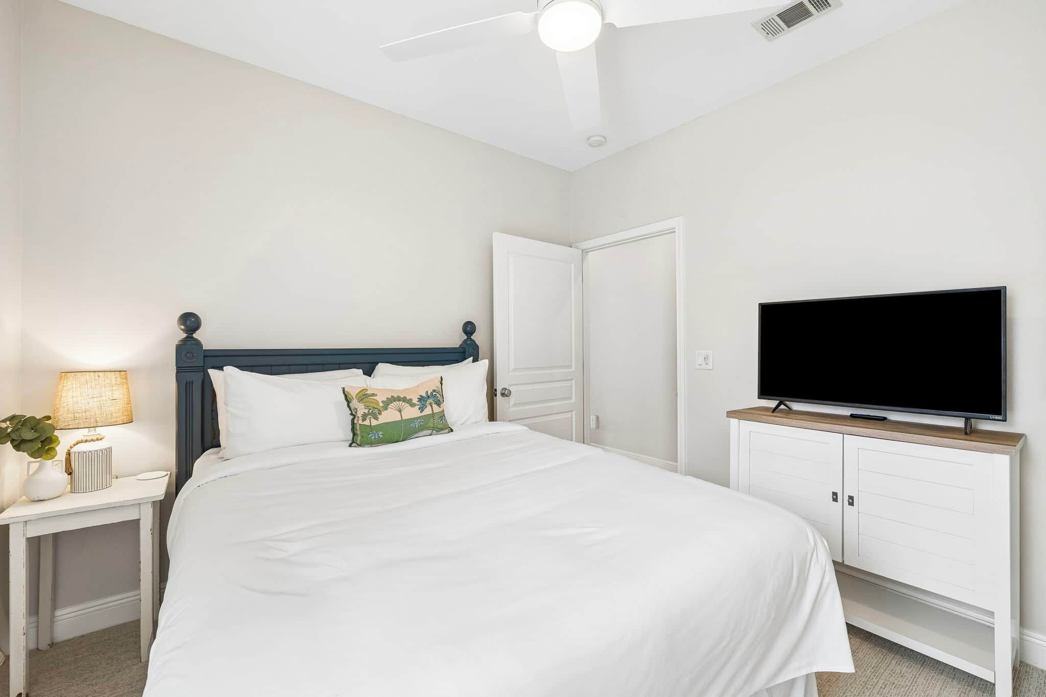 A bedroom with a bed, a nightstand, a lamp, a television, and a ceiling fan.