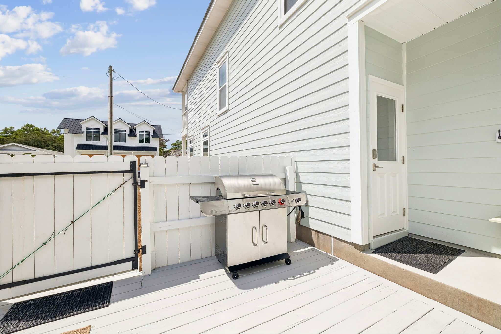 A backyard with a barbecue grill and a white fence.