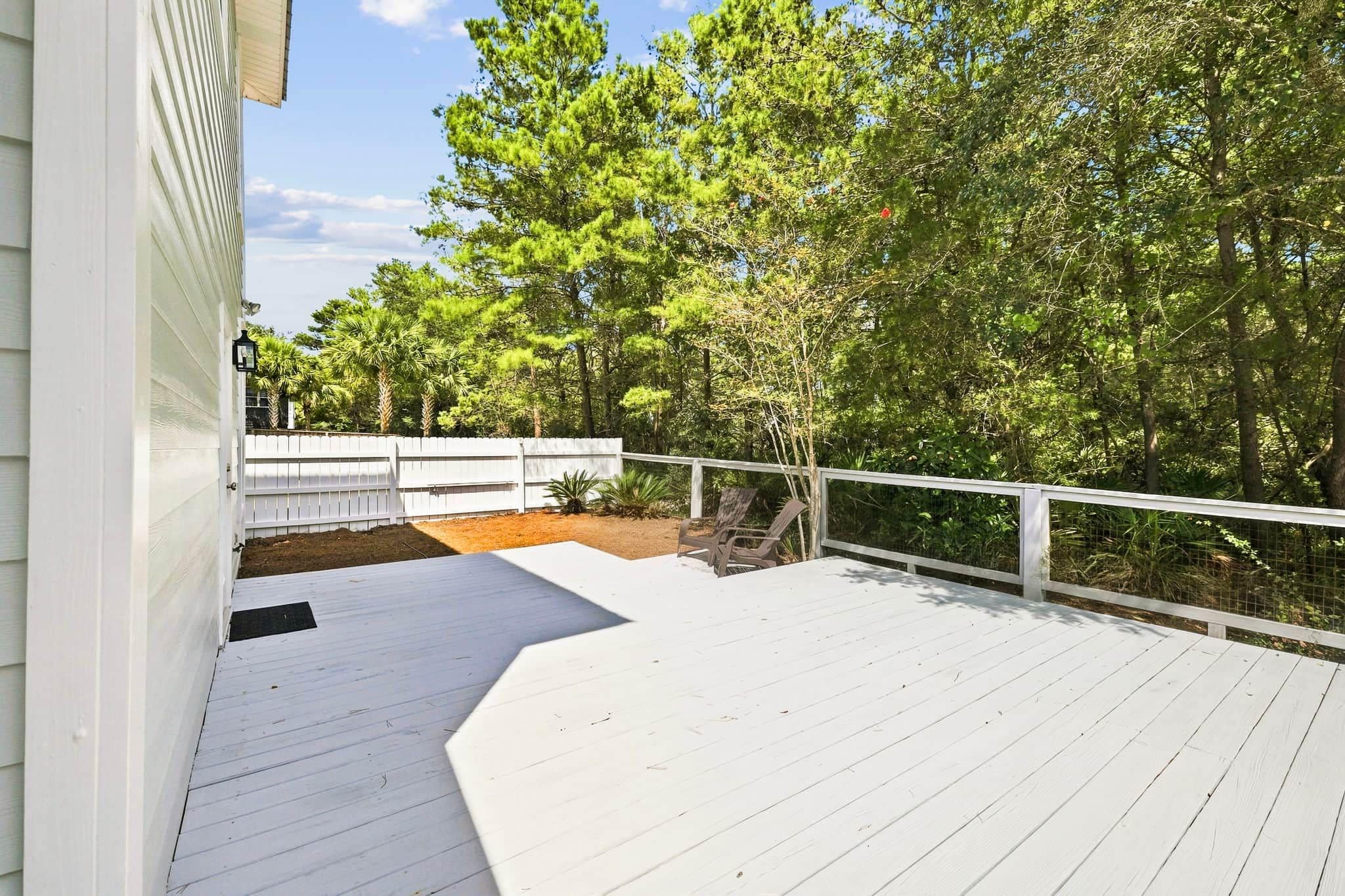 A wooden deck with a white railing, surrounded by trees and a white fence.