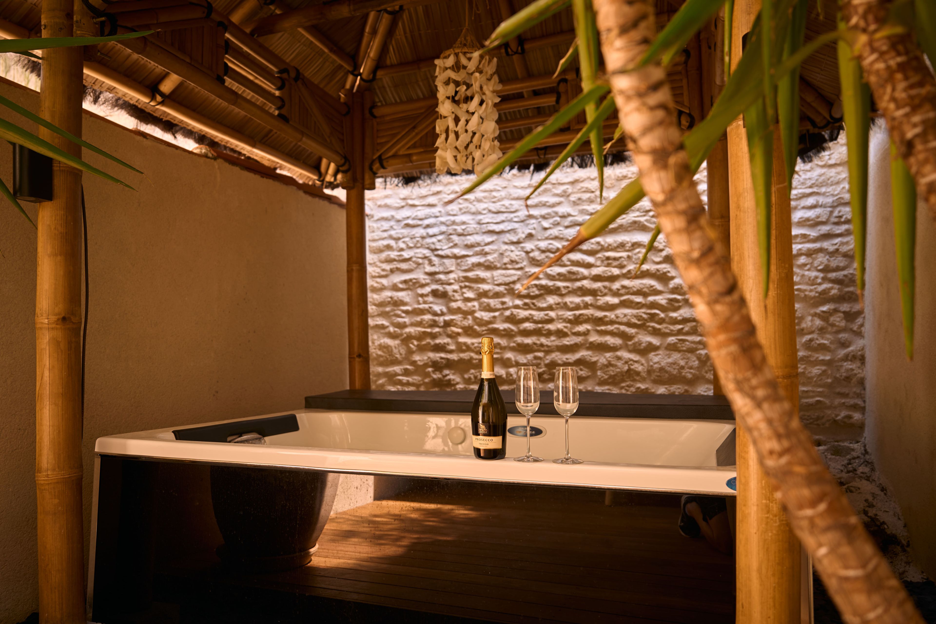 A spa area with a wooden bench, a bathtub, and a bottle of champagne.
