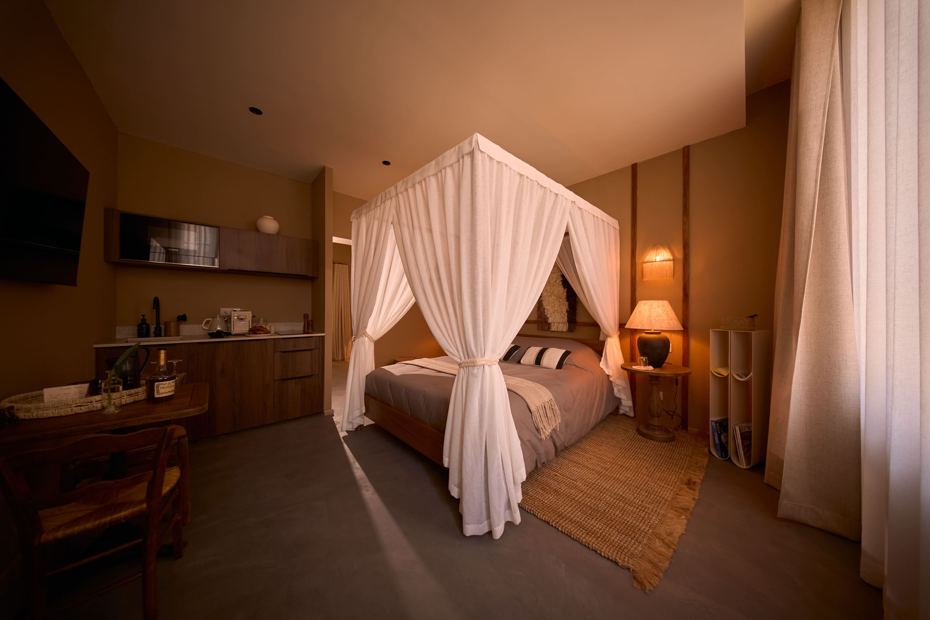 A hotel room with a four-poster bed, a sitting area with a table and chairs, a television, and a minibar.