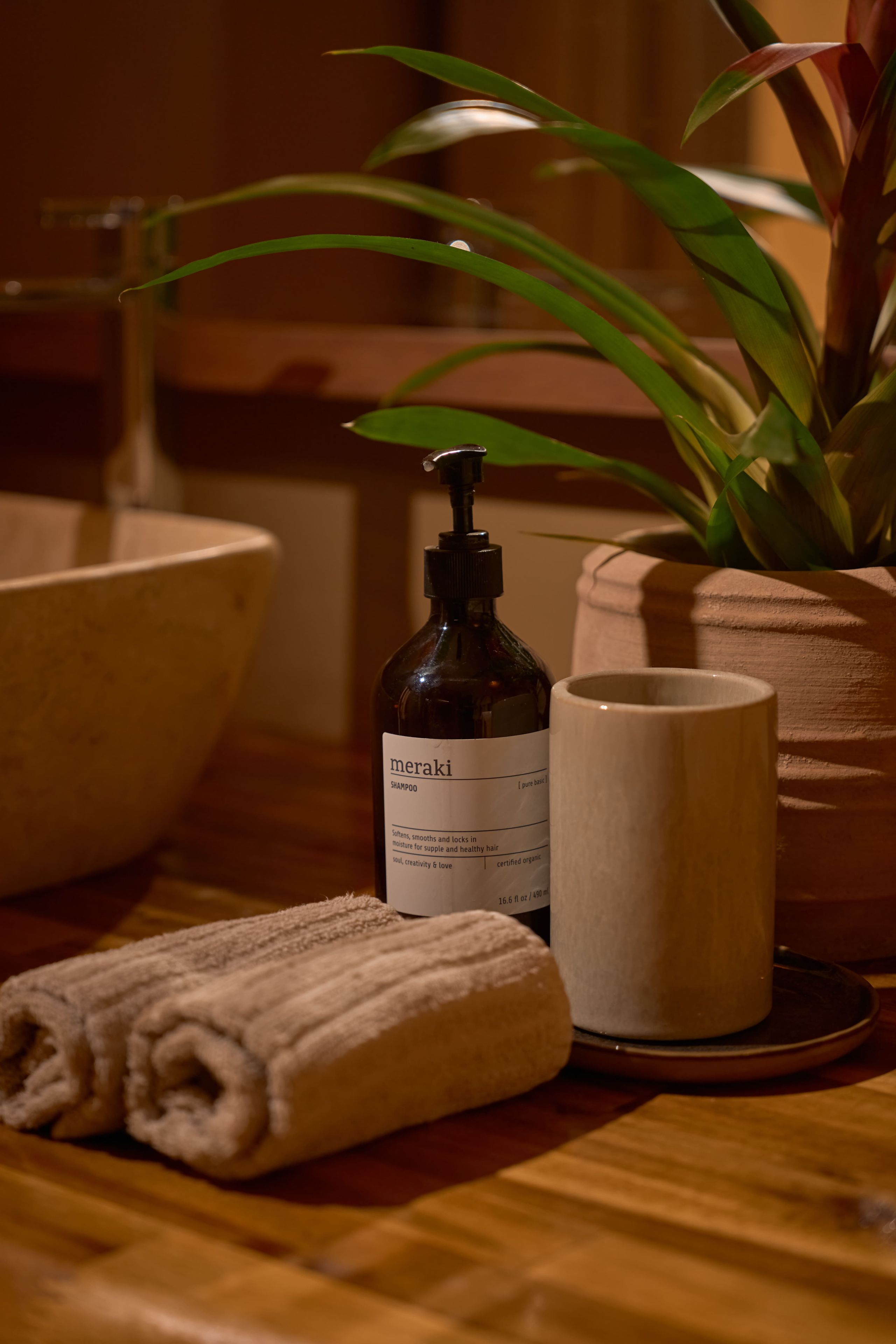 A bathroom setting with a bottle of shampoo, a towel, and a potted plant.