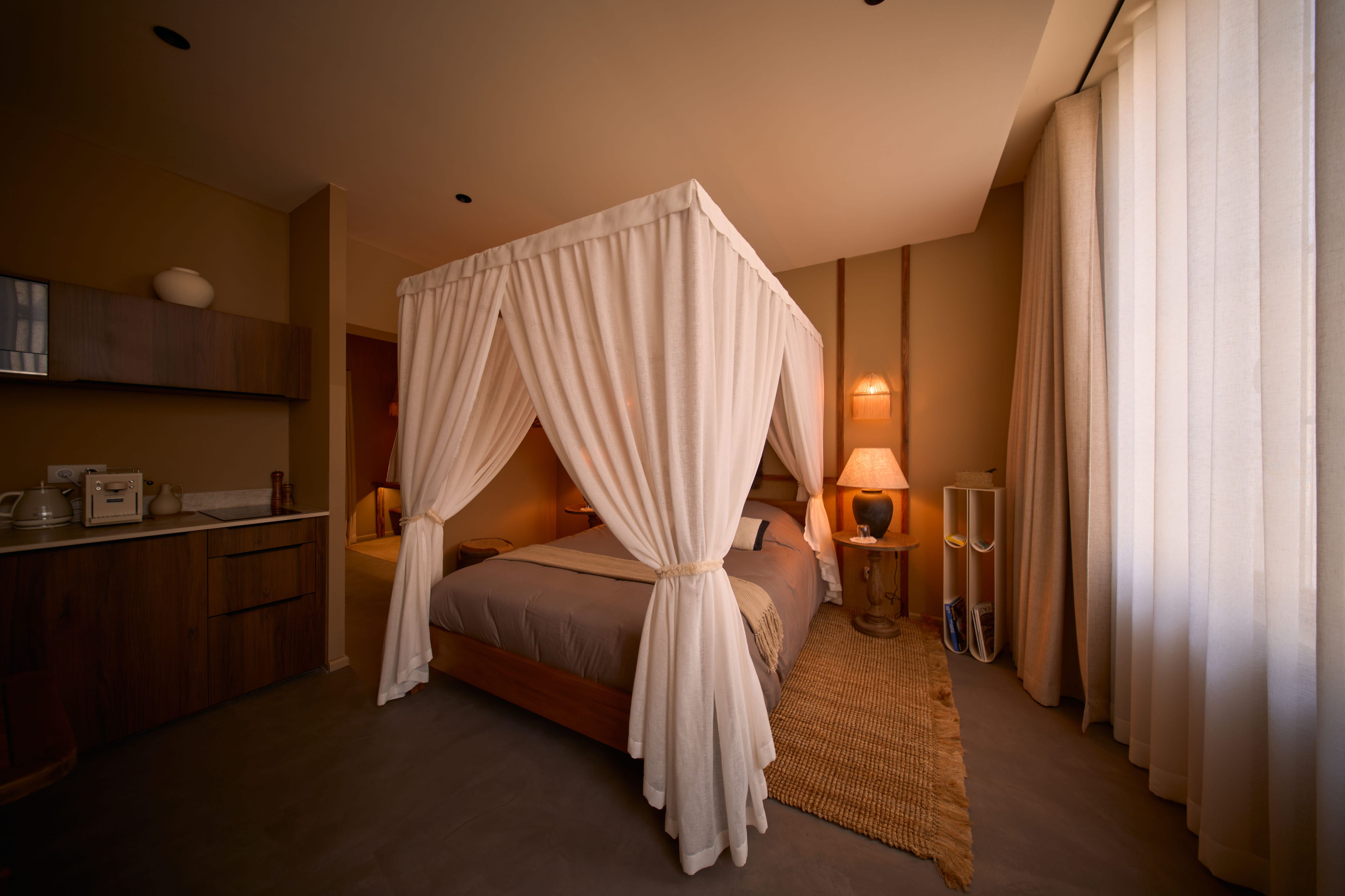 Habitación de hotel con cama con dosel, lámparas de noche, cómoda de madera y una pequeña alfombra.