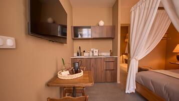 Een compacte hotelkamer met een bed, een kleine kitchenette, een eethoek met een tafel en stoelen, en een aan de muur bevestigde televisie.