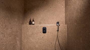 Een douche met een handdouche, een bedieningspaneel aan de muur en twee flessen op een plank.