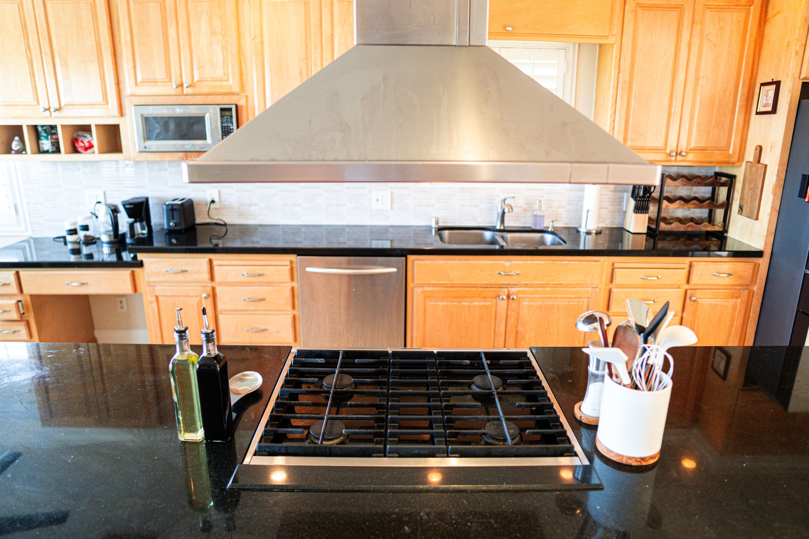 A kitchen with wooden cabinets, a stainless steel range hood, a black countertop, and a sink.