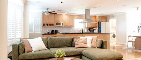 A modern living room with a sectional sofa, a wooden coffee table, and a view of the kitchen in the background.