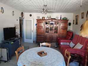 A living room with a television, a dining table with a basket, a red sofa, and a wooden cabinet with glass doors. - Charming 1-bedroom apartment in Nice (Nice)