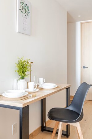 A dining area with a wooden table, white plates, cups, and a black chair. - Aura 41 Un refugio sobre Reforma (Ciudad de México)