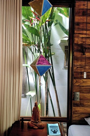 Quarto com uma janela grande, uma planta, um adorno pendurado e uma pequena estátua de Buda.