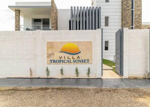 A gated entrance to a property named 'Villa Tropical Sunset' with a modern design and a logo featuring a sun and waves. - 10br Luxury Villa Private Pool (Sosúa)