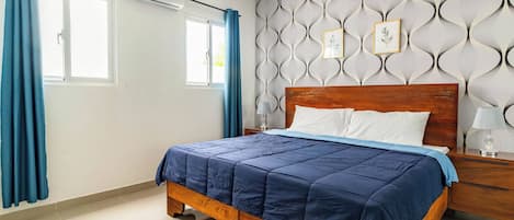 A bedroom with a wooden bed, a nightstand, a wall-mounted air conditioner, and a window with curtains.