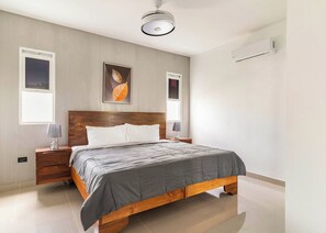 A modern bedroom with a wooden bed frame, a grey bedspread, two bedside tables with lamps, and a ceiling light fixture. - 10br Luxury Villa Private Pool (Sosúa)