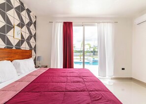 Une chambre d’hôtel comprenant un lit, une table de chevet, une lampe, une vue sur une piscine et un motif géométrique sur le mur.
