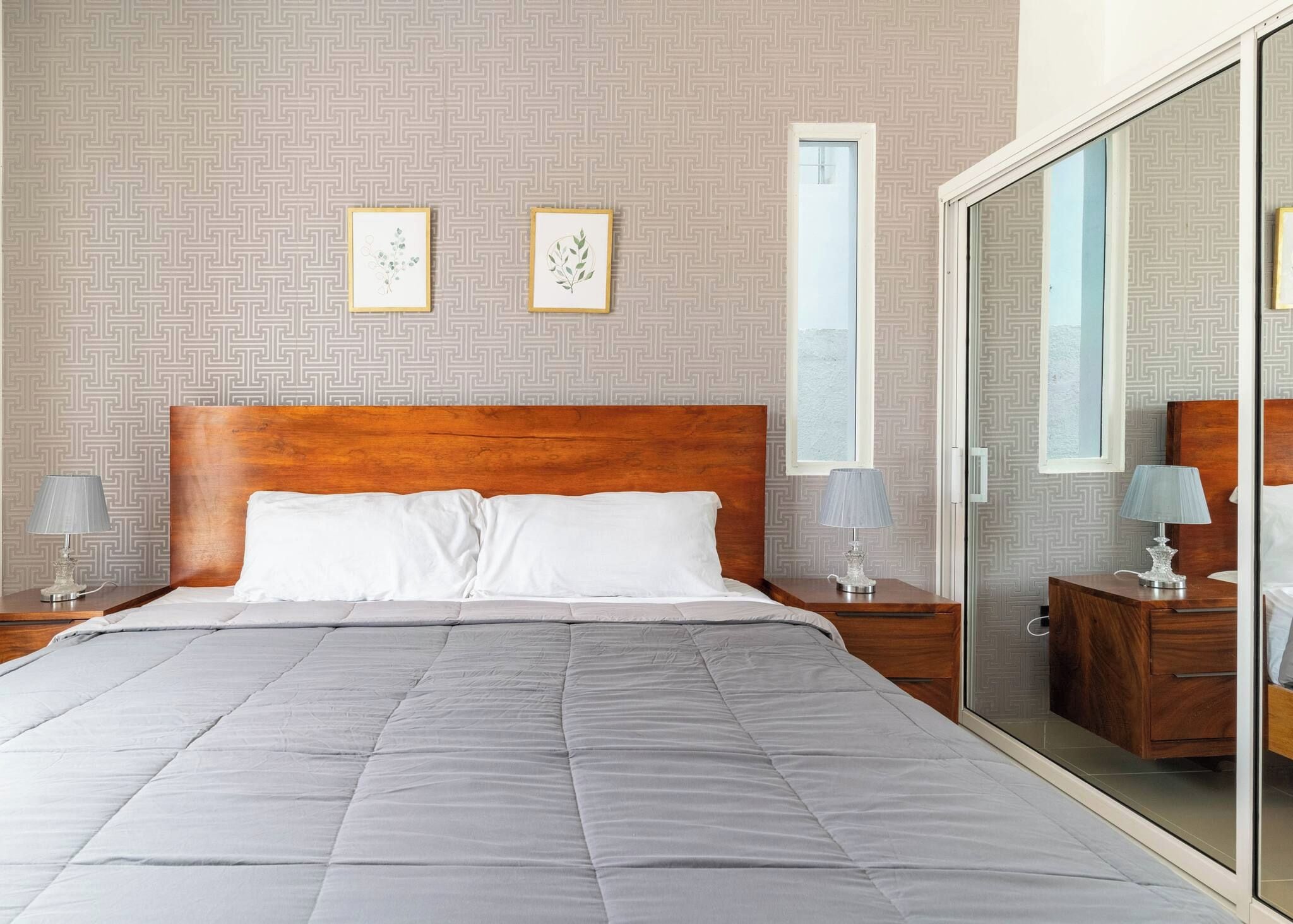 Una habitación de hotel con una cama grande, dos mesitas de noche con lámparas, un armario con espejo y una pared con estampado.