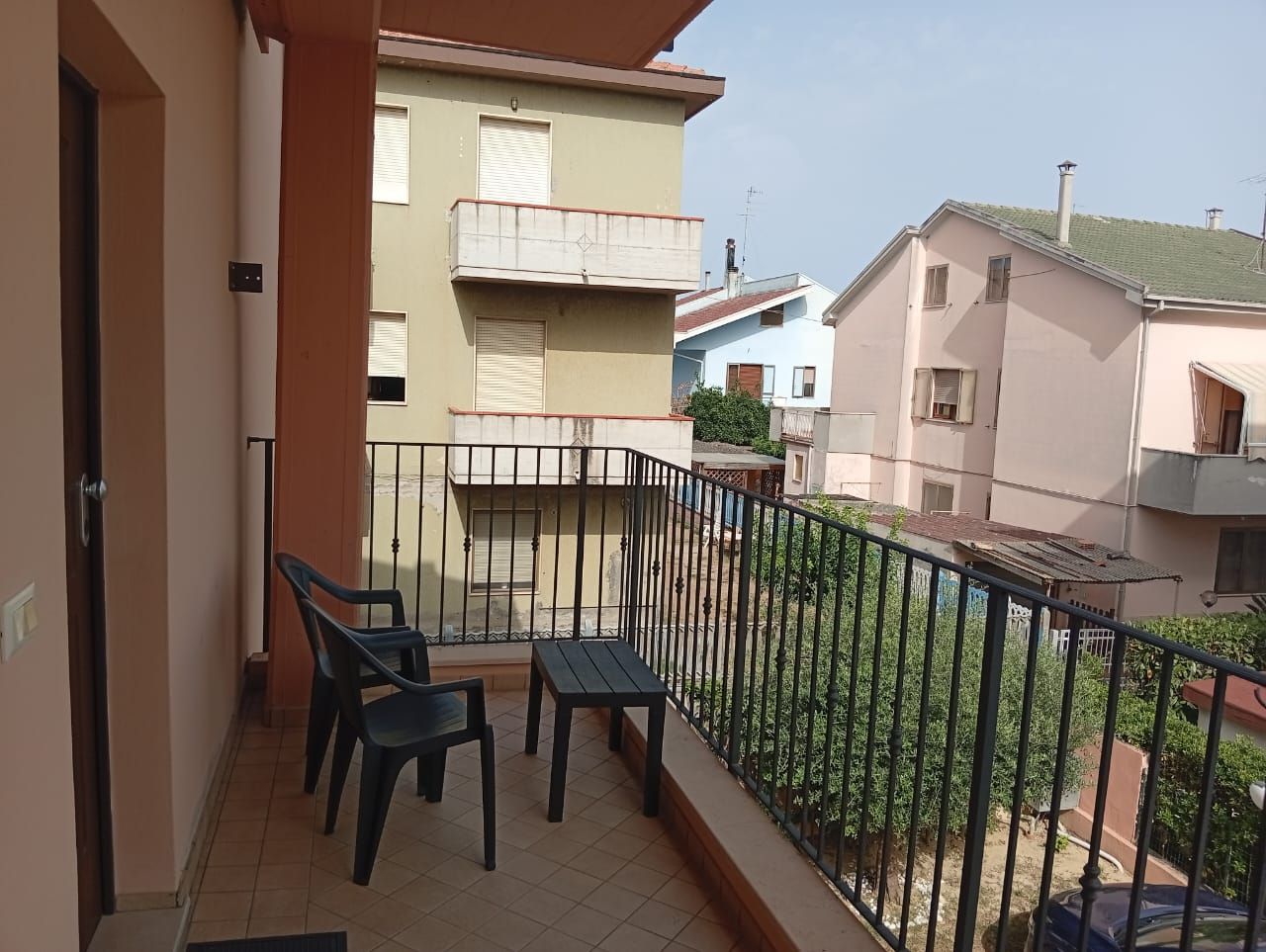 Een balkon met twee stoelen en een tafel, met uitzicht op omliggende gebouwen.