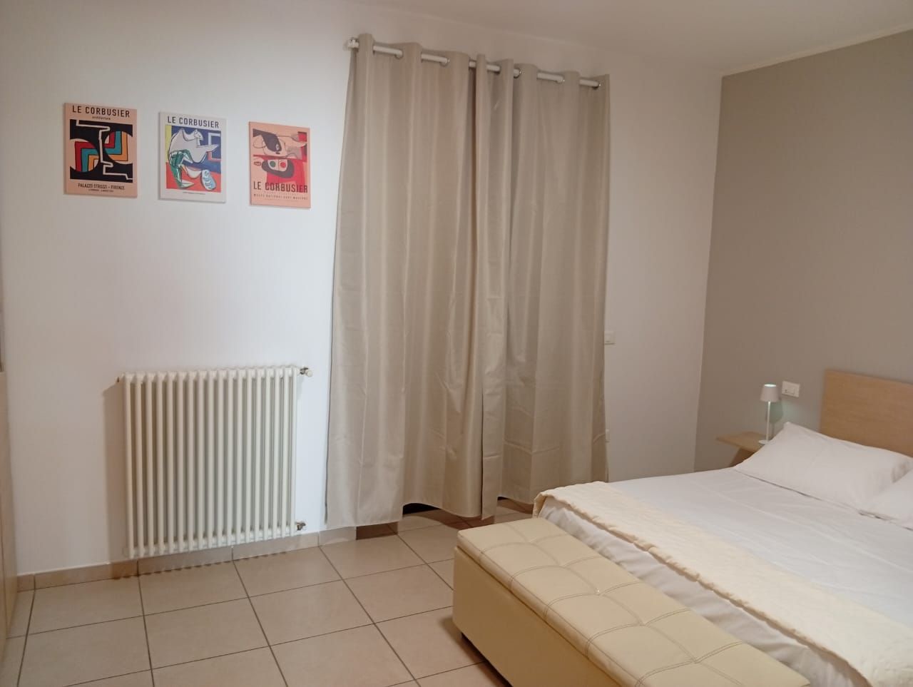 Een slaapkamer met een bed, een radiator, gordijnen en drie posters aan de muur.