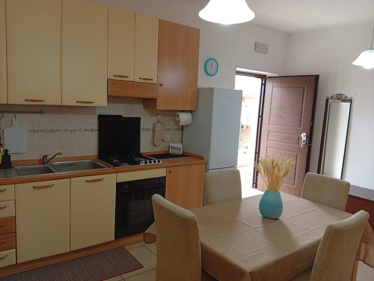 Een keuken met een eettafel, stoelen, een klok en een koelkast.