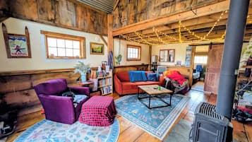 A cozy cabin interior with a wooden ceiling, a sofa, a chair, a table, and a fireplace.