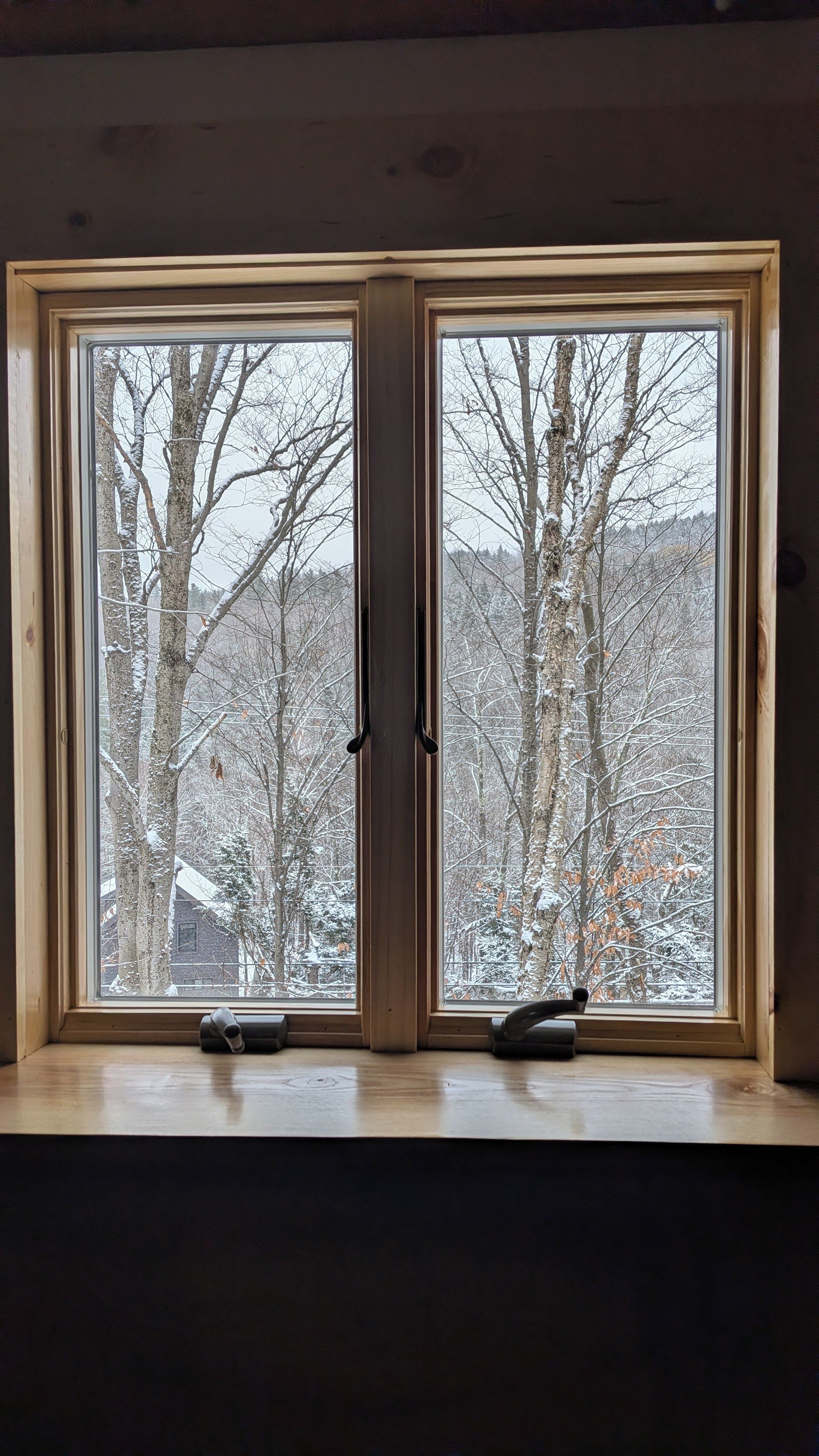 A room with a large window featuring a view of snow-covered trees and a distant building.
