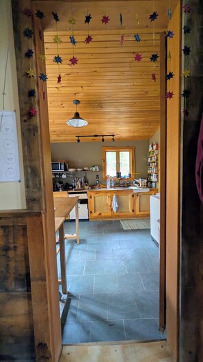 A kitchen with wooden cabinets, a microwave, and a window. - Rustic Cabin up against Slide Brook, on Sugarbush Resort (Waitsfield)