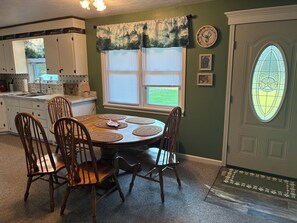 A dining area with a round table, six wooden chairs, and a window with blinds.